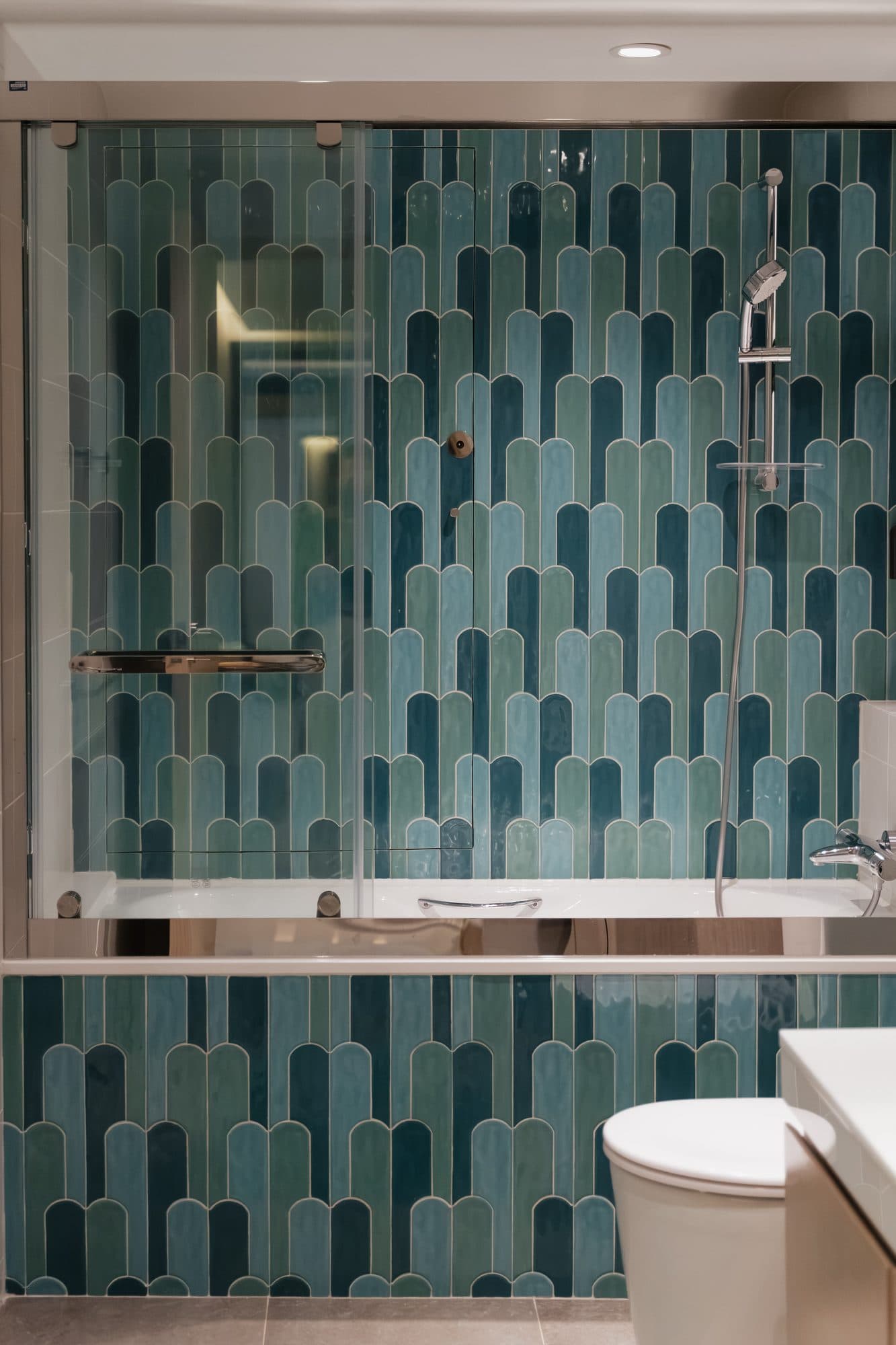 The bathroom tiled floor to ceiling in teal arch-shaped glazed tile, with a glass screen over the bath