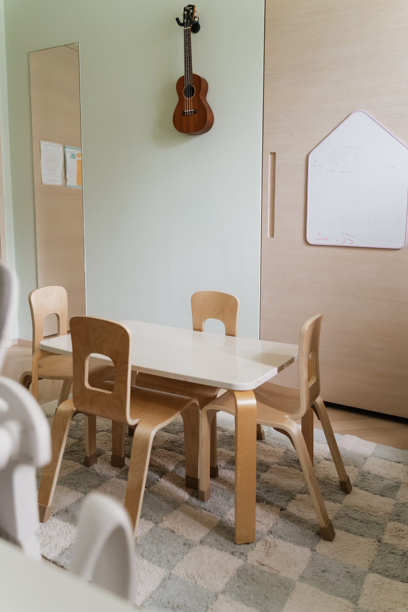 A play corner with a full-length mirror, a ukulele on the wall and a house-shaped drawing panel set into pale timber joinery