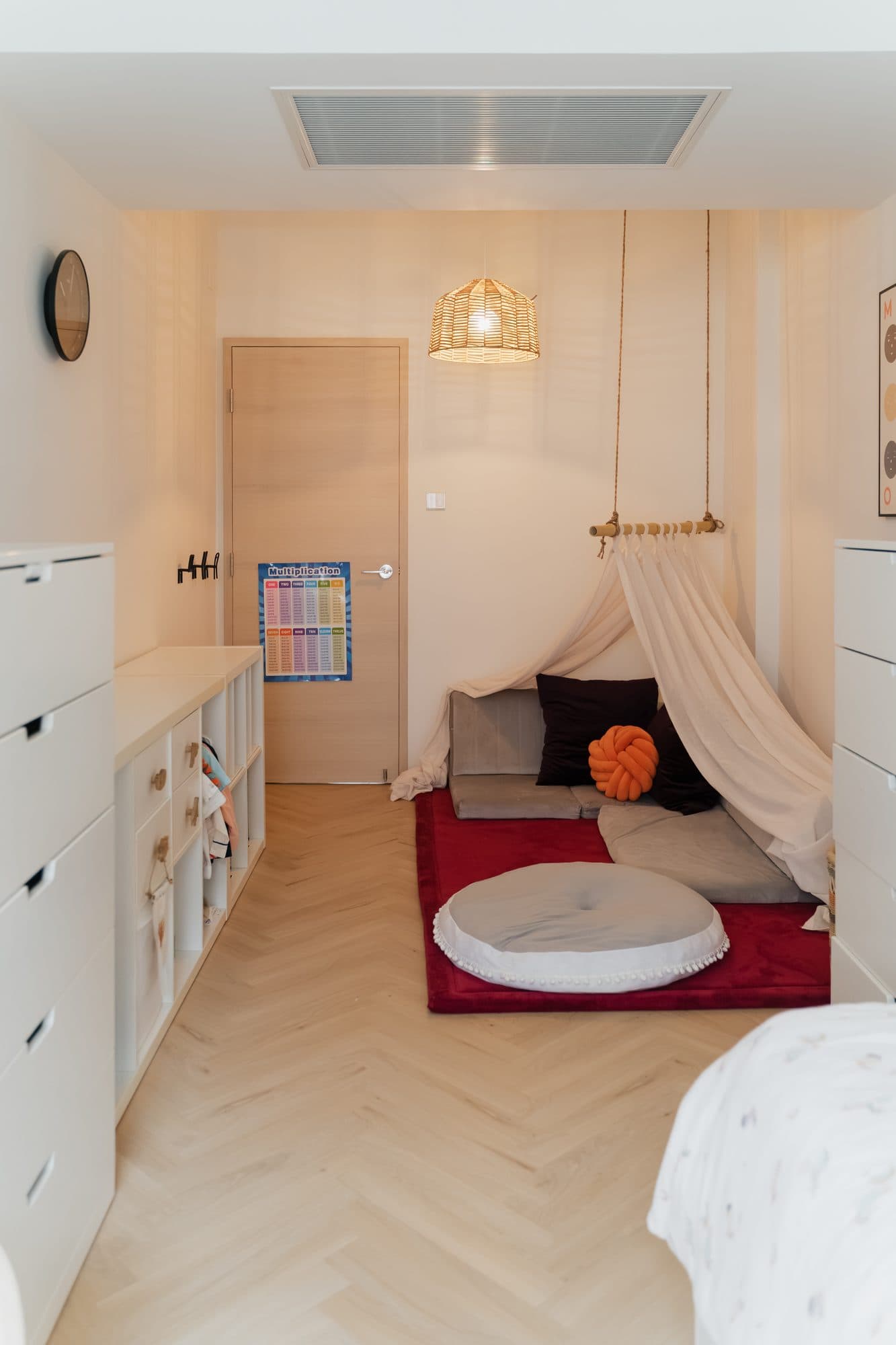 A child's bedroom in pale timber: low cube storage the length of one wall, ending in a canopied bed nook over a red rug