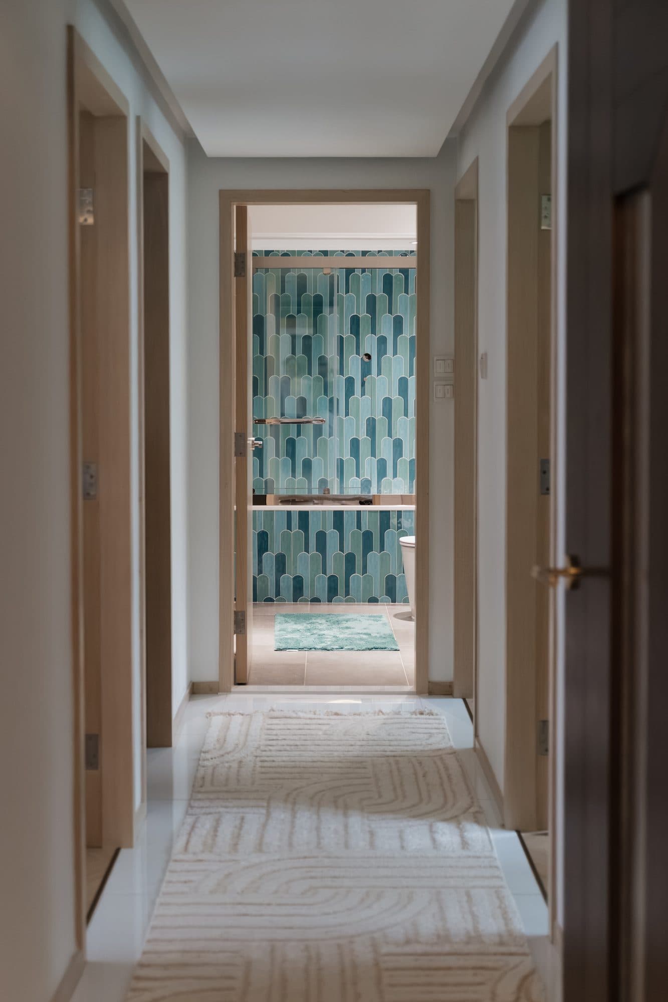 The corridor of pale timber doors, looking through an open door to the teal-tiled bathroom at the end