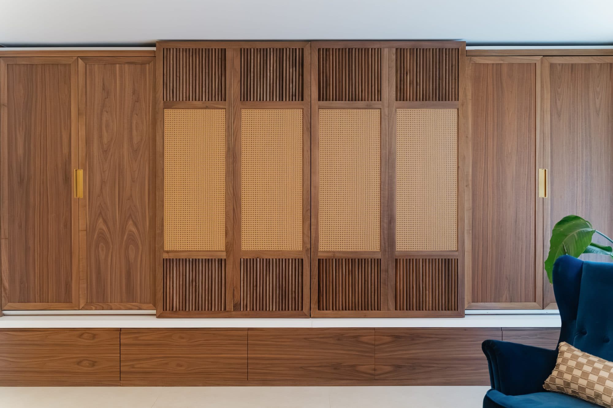 The living room joinery wall closed: walnut sliding doors with louvered bands above and below woven rattan panels, over a low run of drawers