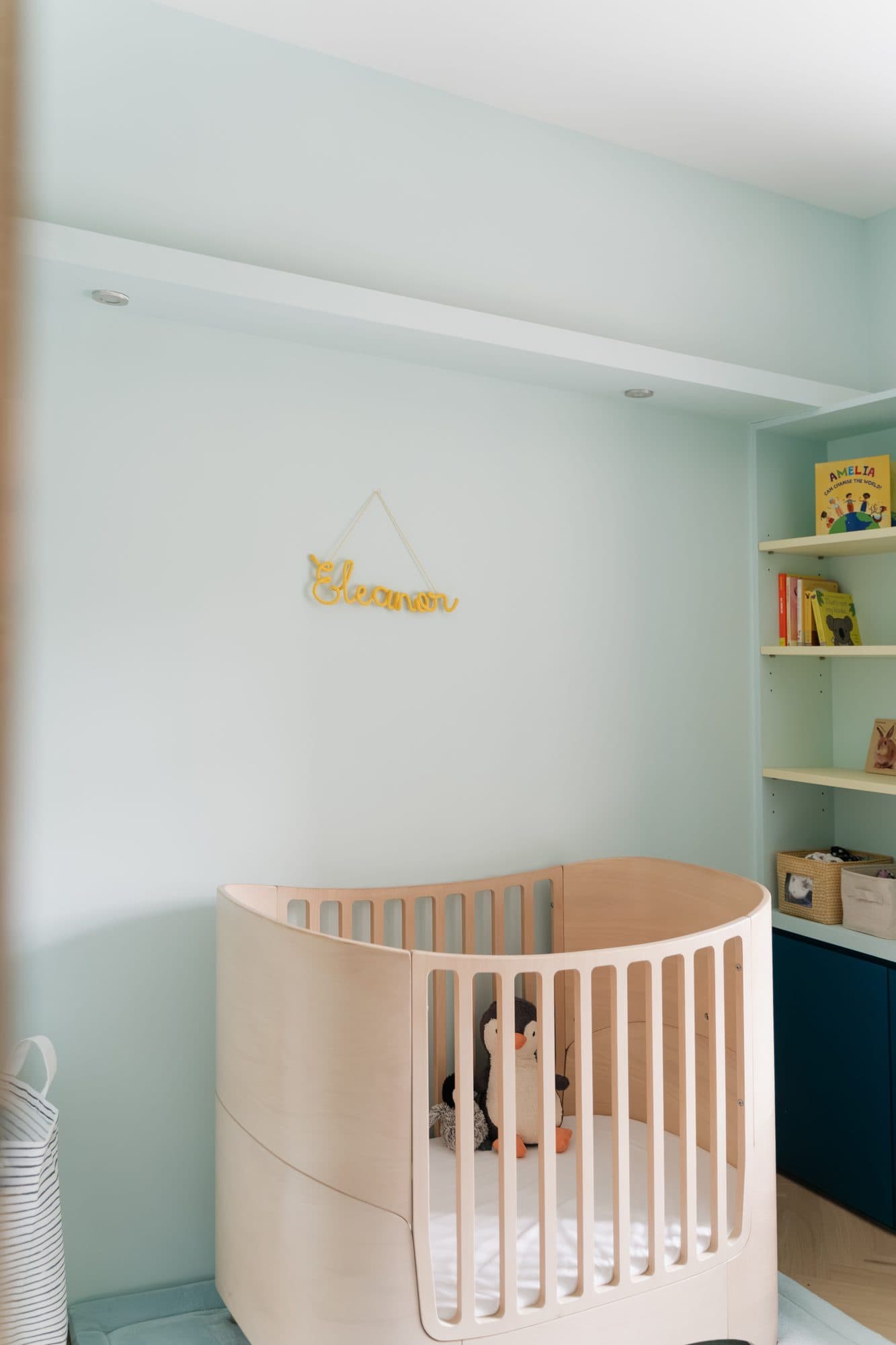 The nursery in soft mint: a curved birch cot beside built-in shelving over deep blue cabinetry