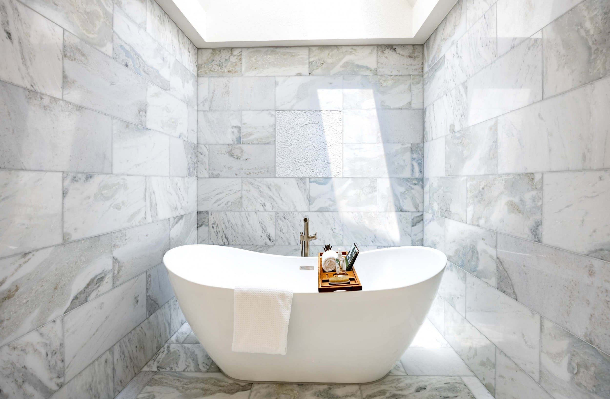 Freestanding tub under a skylight in a marble-lined bathroom